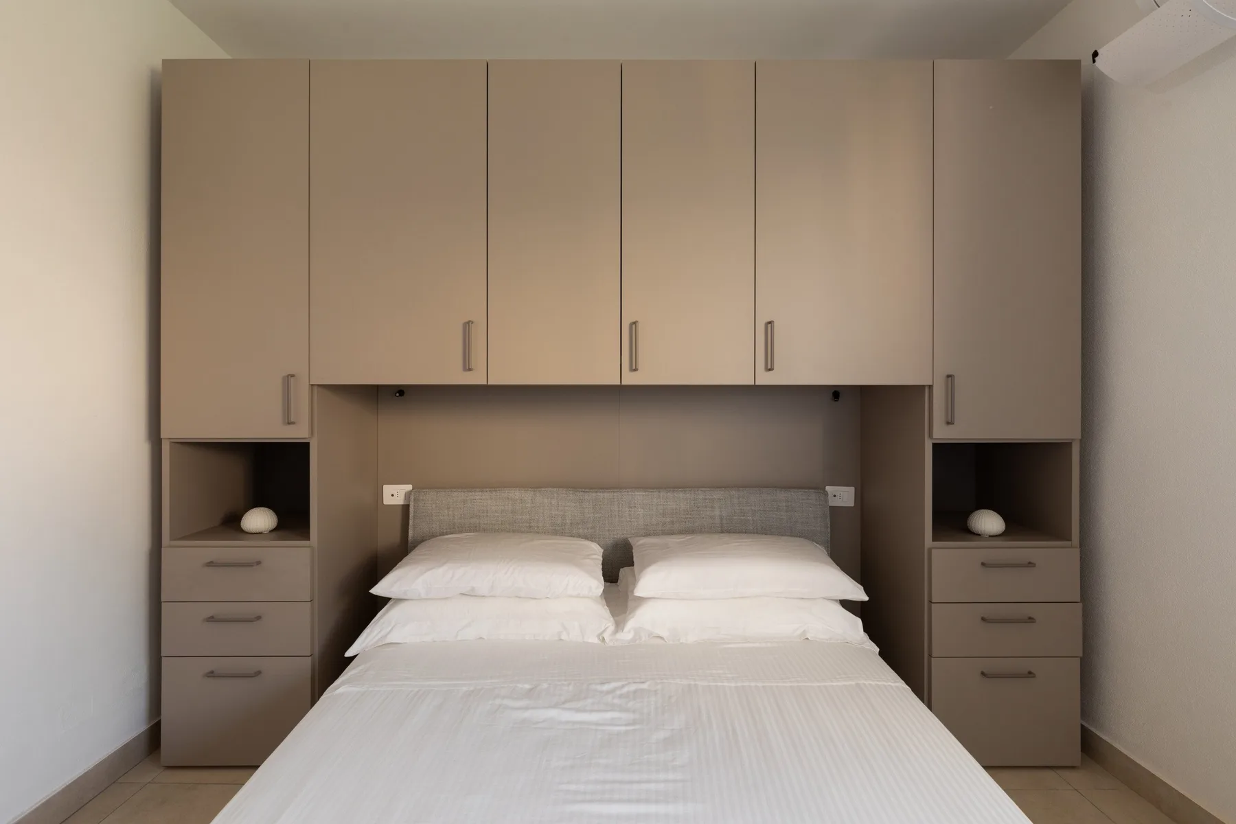Dormitorio con una cama bajo armarios empotrados y estantes laterales.