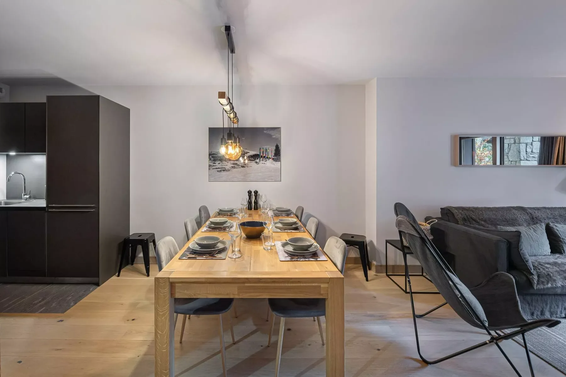 Comedor con una mesa de madera junto a una cocina oscura y asientos de sala.