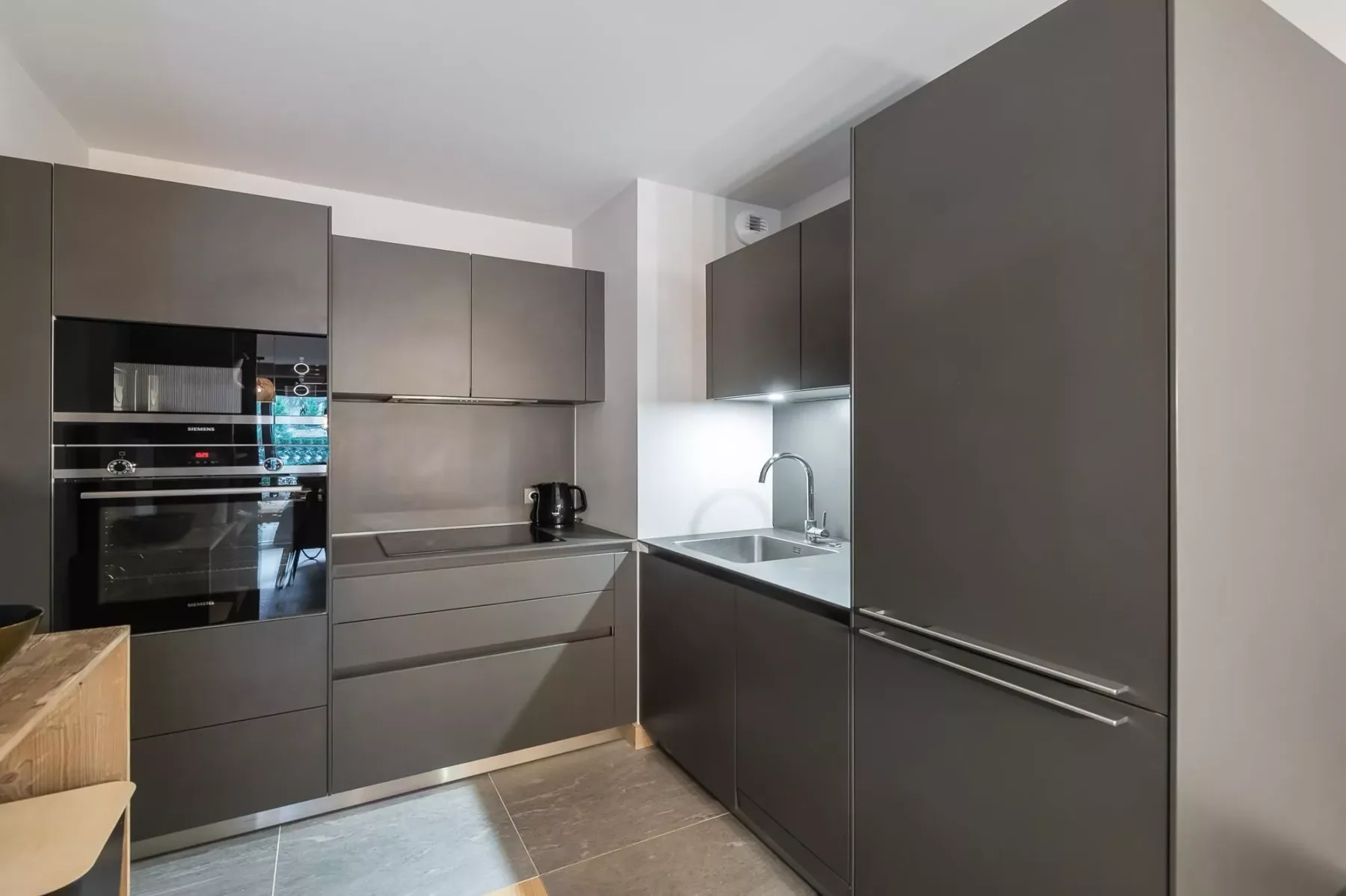 Una cocina moderna con armarios oscuros, electrodomésticos integrados y un fregadero.