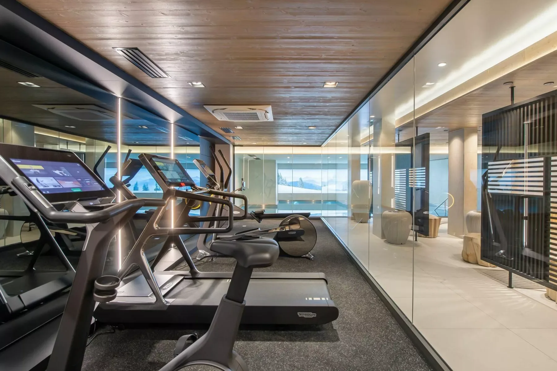 Un gimnasio con cintas de correr junto a una zona de estar acristalada.