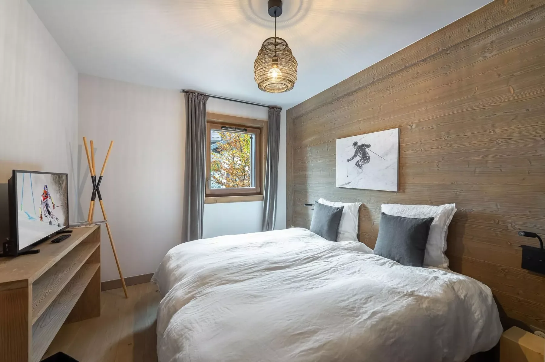Un dormitorio con una cama, una ventana y un televisor sobre un mueble bajo.