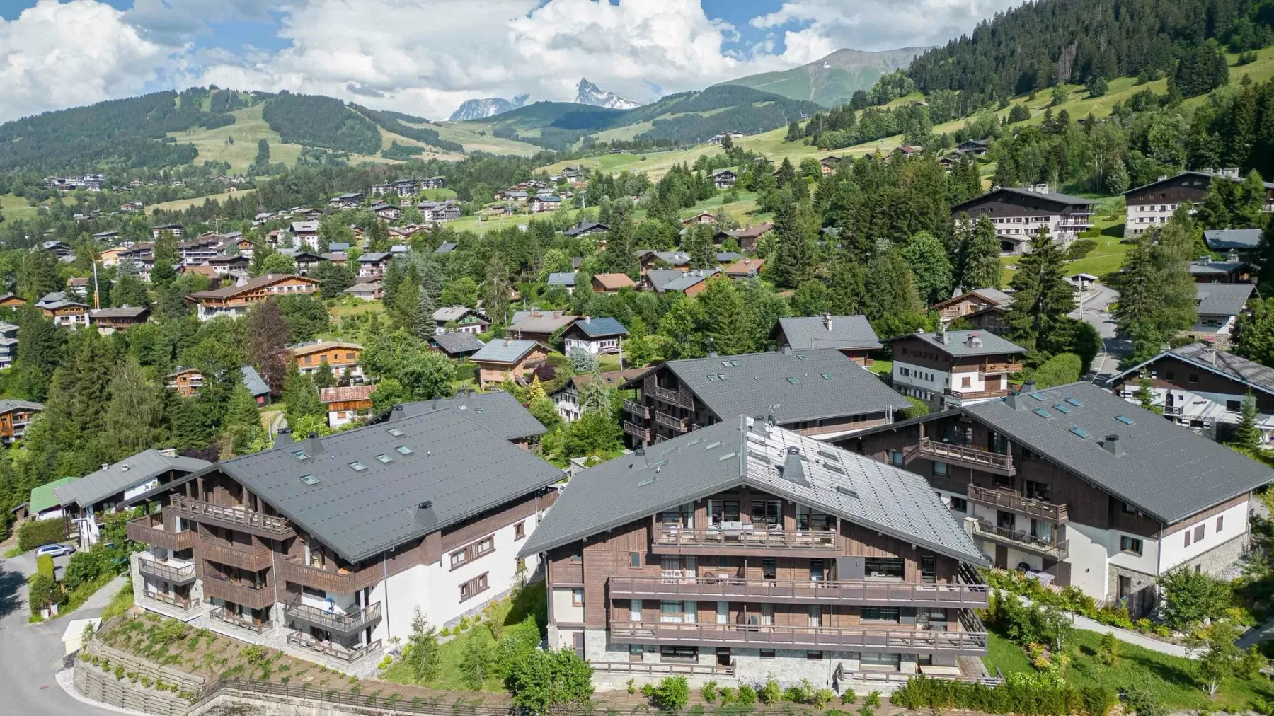Un pueblo de montaña con edificios tipo chalet se extiende entre laderas verdes y árboles.