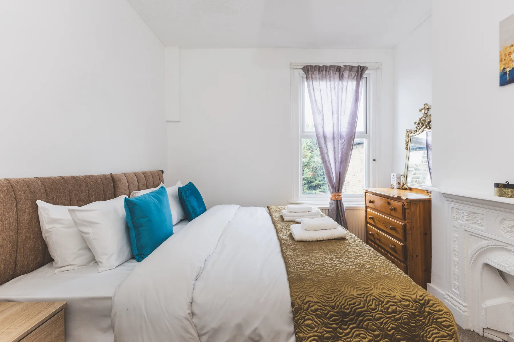 A bedroom with a neatly made bed and a wooden dresser beside the window.