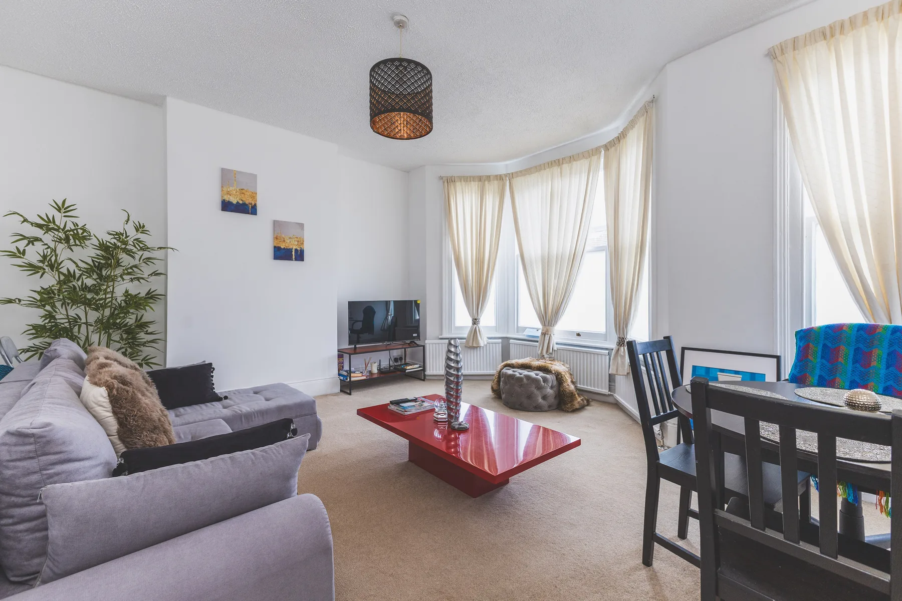 A bright living room with seating, a television, and large curtained windows.