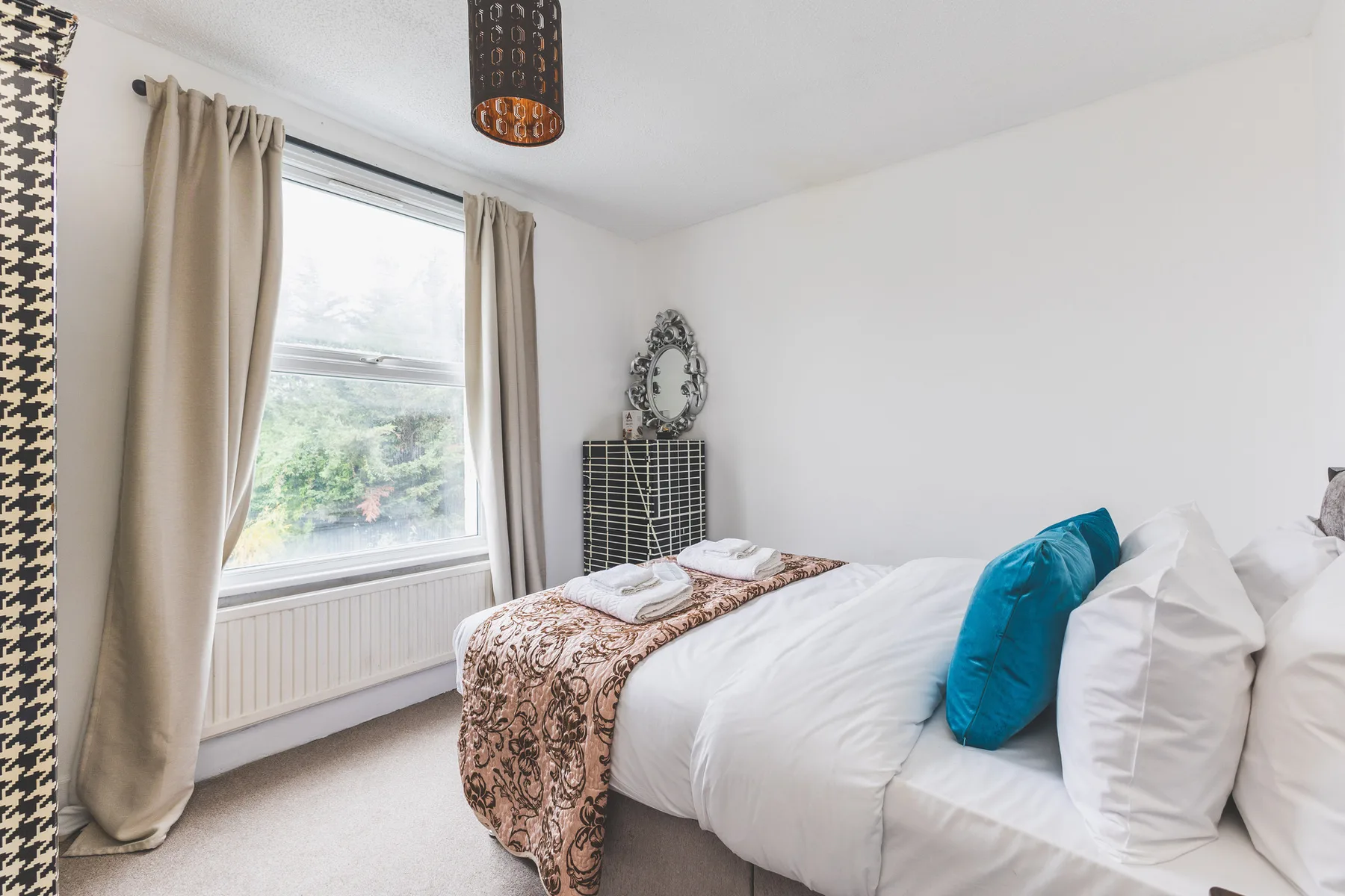 A bright bedroom with a neatly made bed beside a window.
