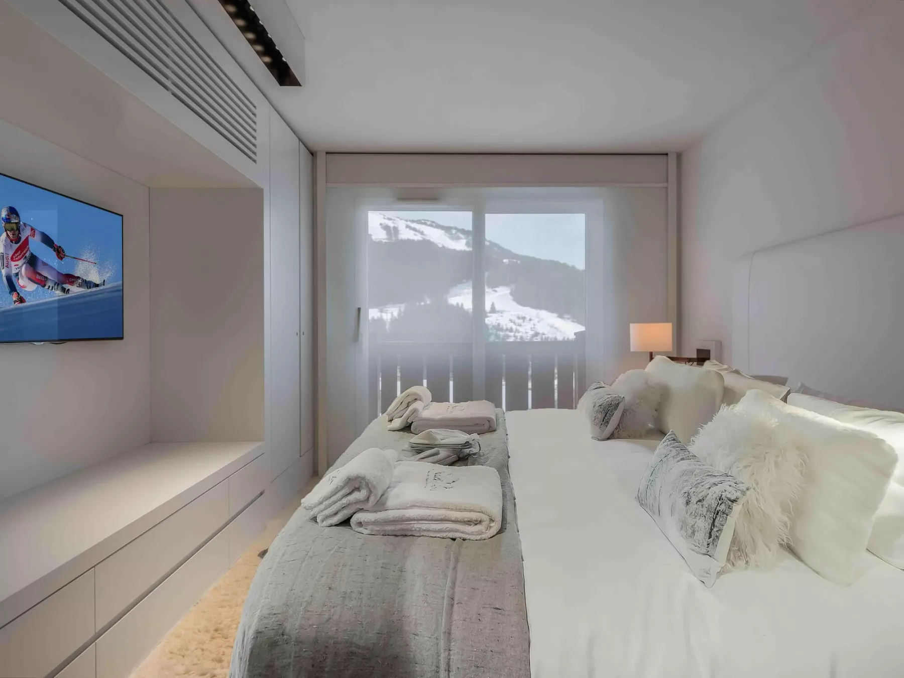 Un dormitorio con una cama grande, ropa de cama en tonos neutros y un televisor montado en la pared.