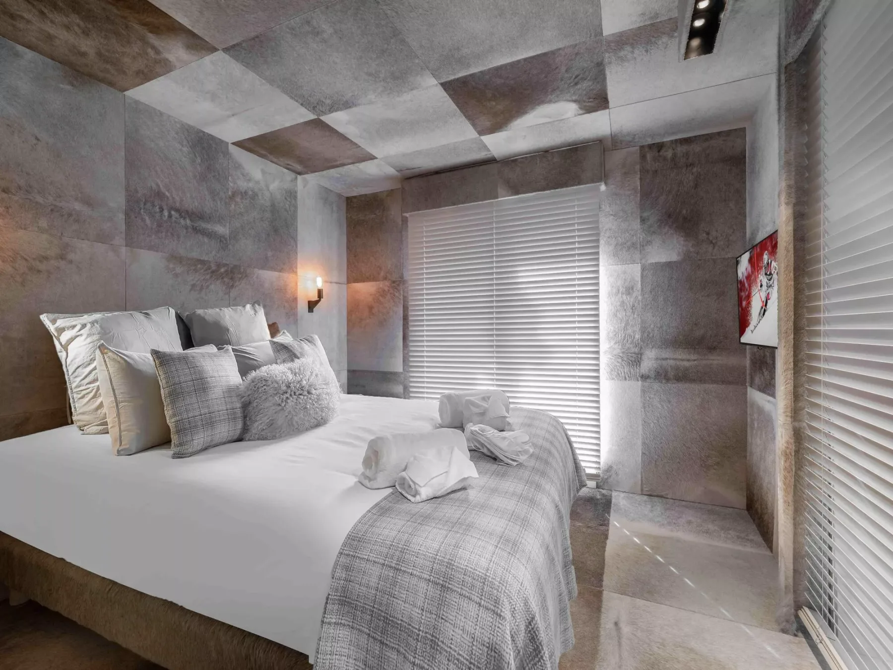 Un dormitorio con una cama tendida y ropa de cama estampada junto a una ventana con persianas.