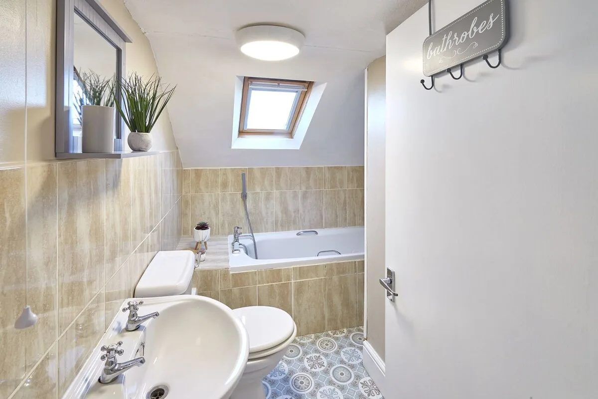A tiled bathroom with a bathtub, sink, and skylight.
