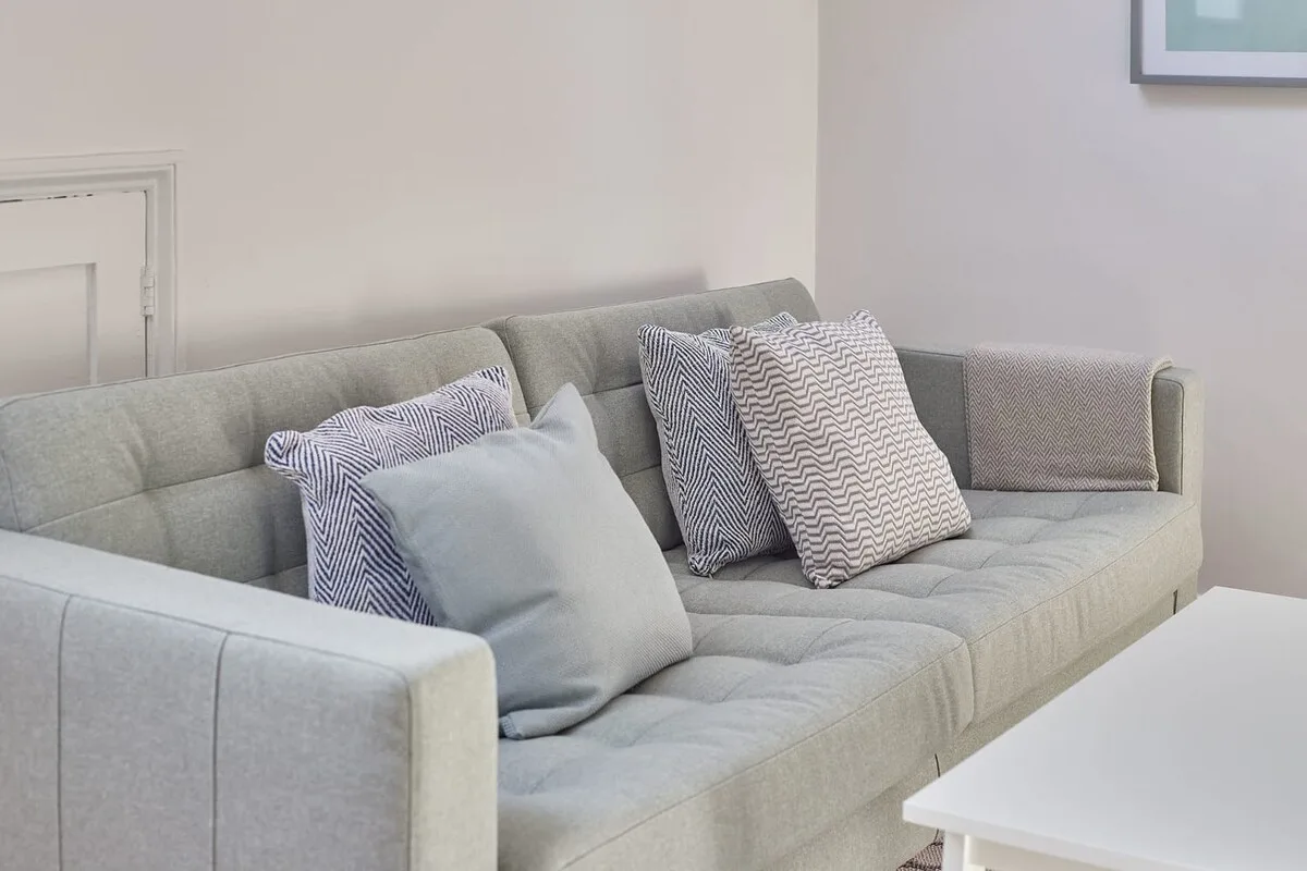 A light-colored sofa with patterned cushions sits beside a white table.