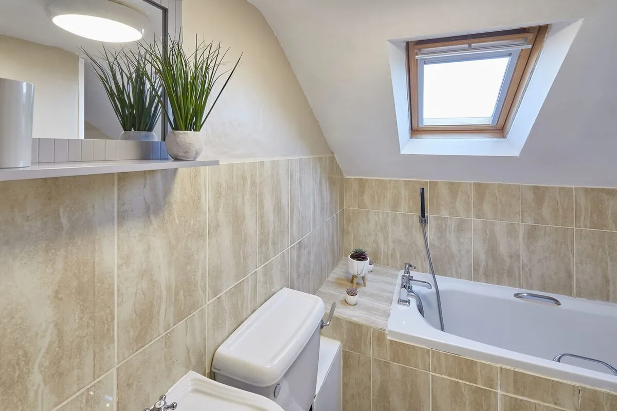 A tiled bathroom with a bathtub beneath a skylight.