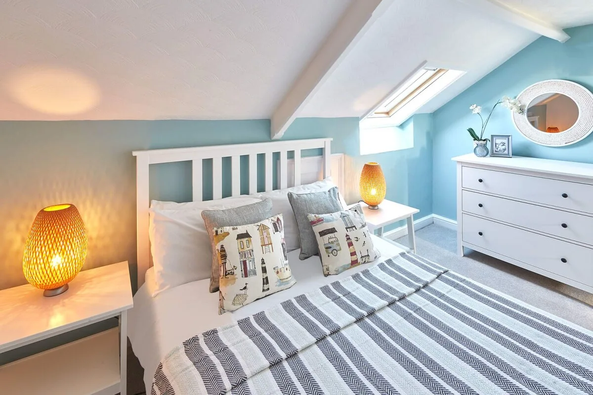 A bright bedroom with a white bed, striped bedding, and a dresser.