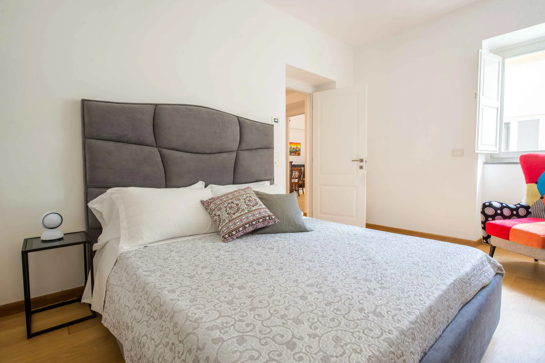 Un dormitorio luminoso con una cama grande y una ventana junto a asientos coloridos.