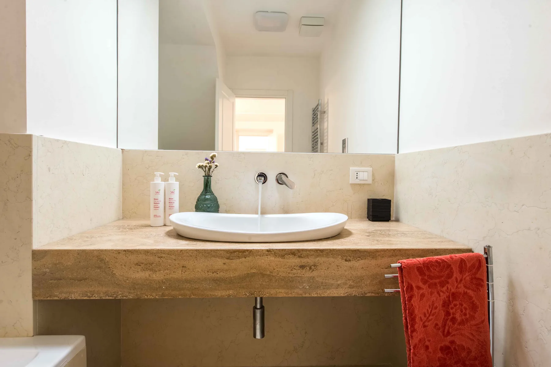 Un tocador de baño con lavabo blanco sobre encimera, espejo grande y toalla roja.