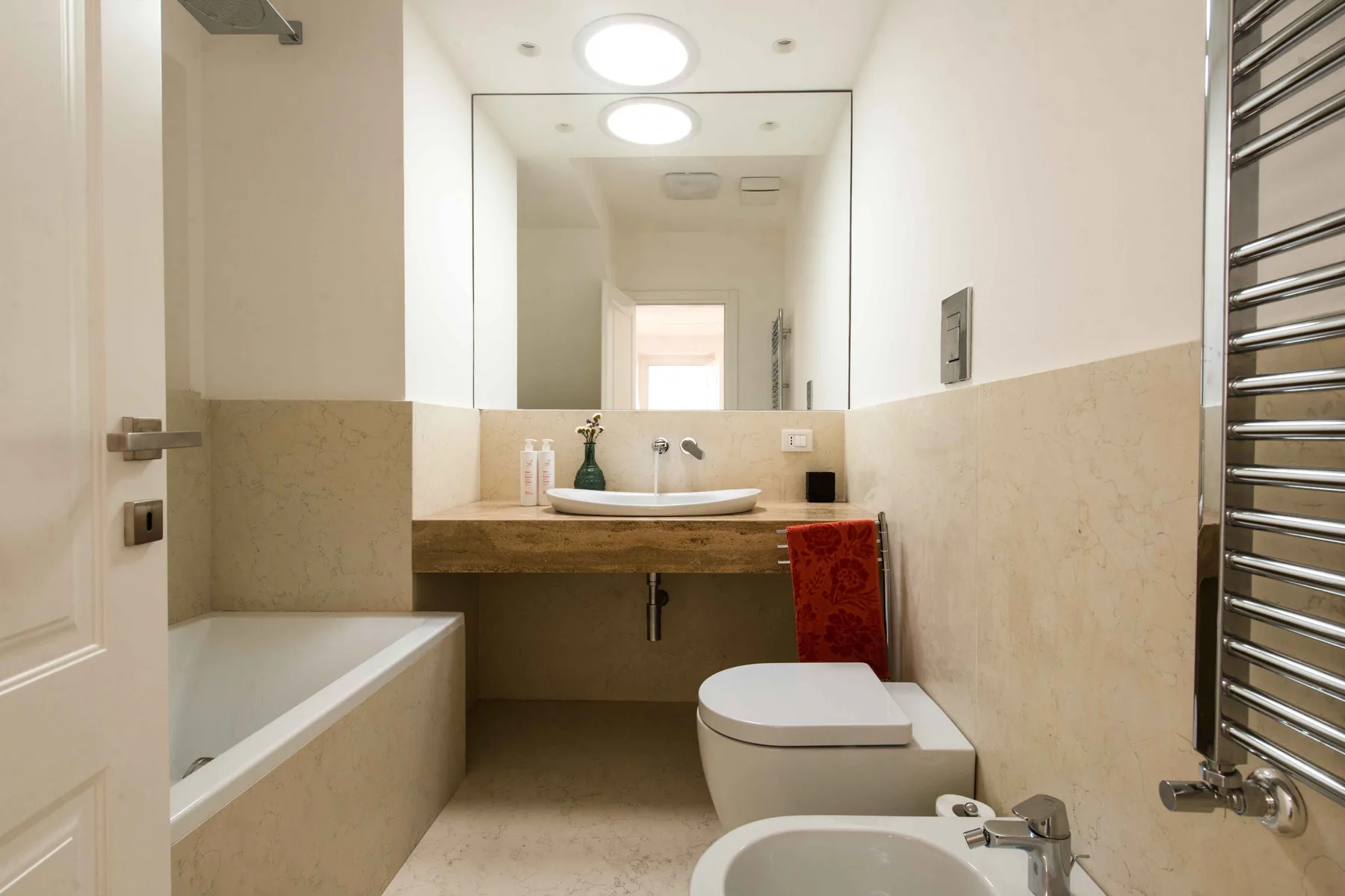 Un baño luminoso con bañera, inodoro y lavabo bajo un espejo grande.