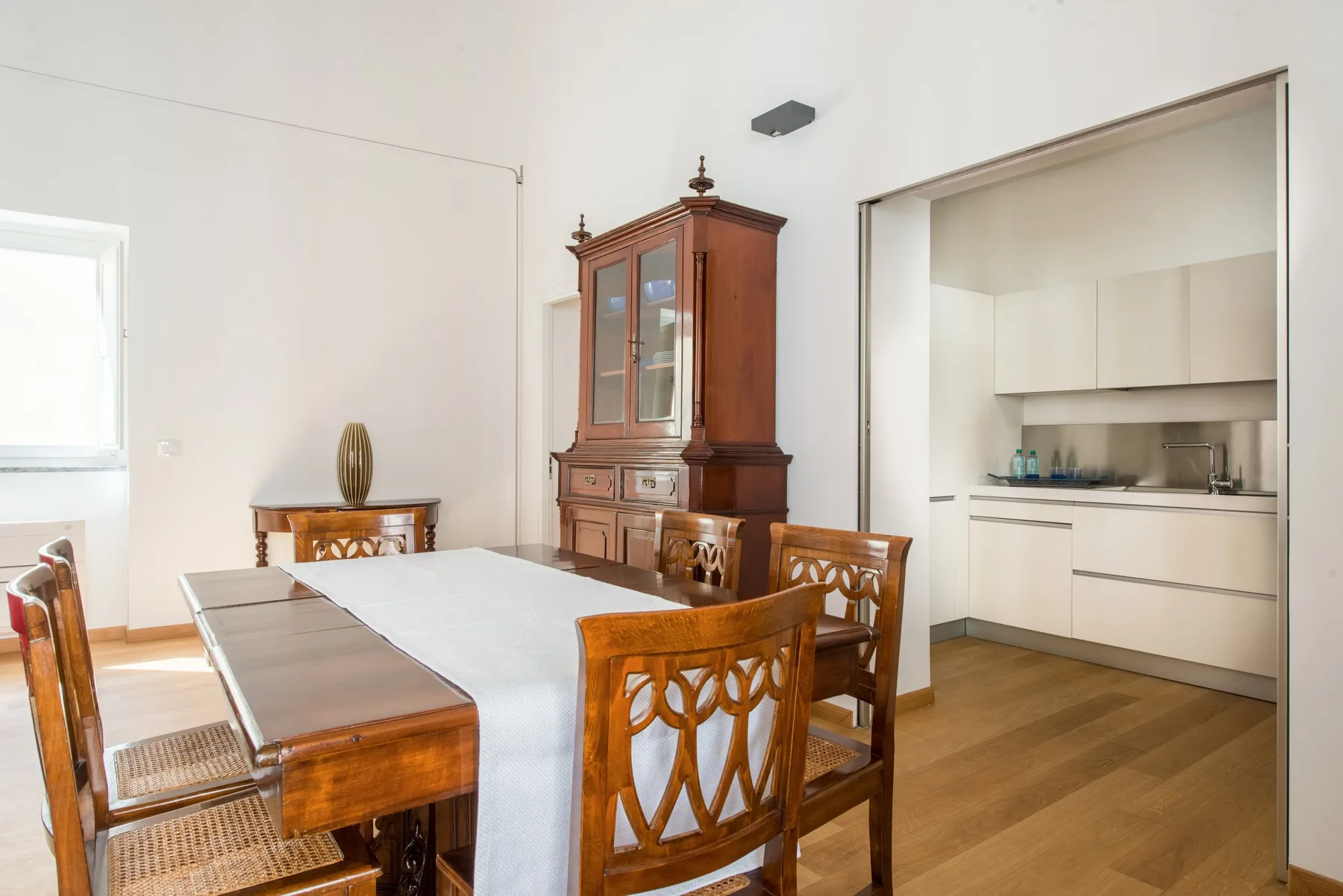 Un comedor con una mesa larga y sillas de madera junto a una cocina abierta.