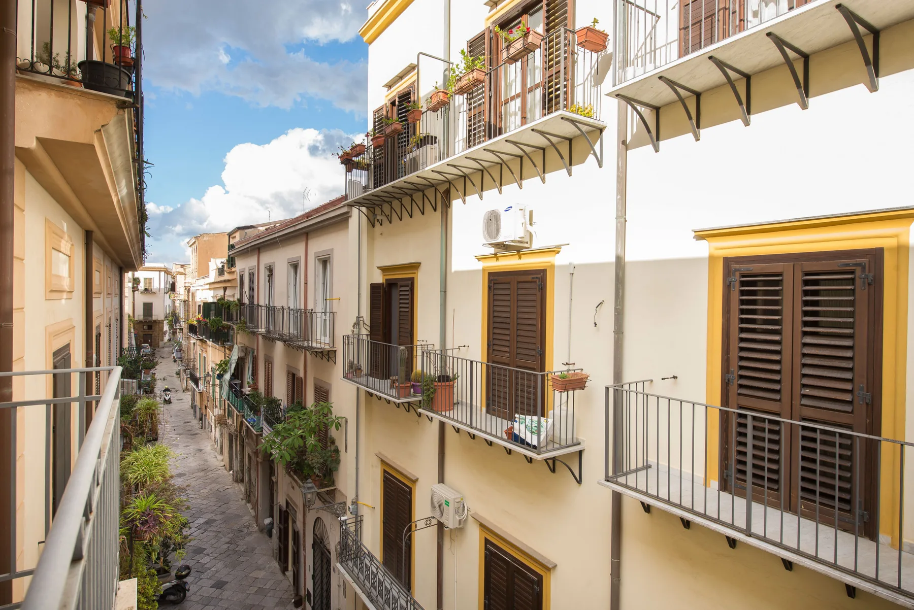Una calle estrecha transcurre entre edificios de apartamentos cercanos con balcones y plantas.