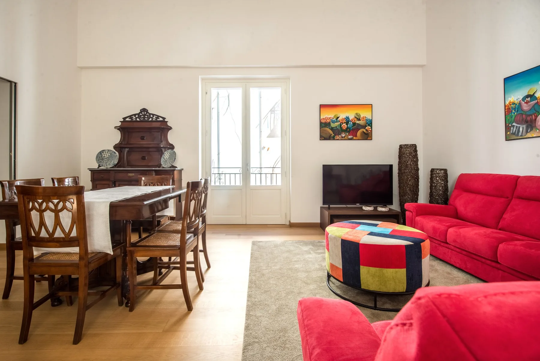Una sala de estar y comedor con asientos de madera, un televisor y un sofá rojo.