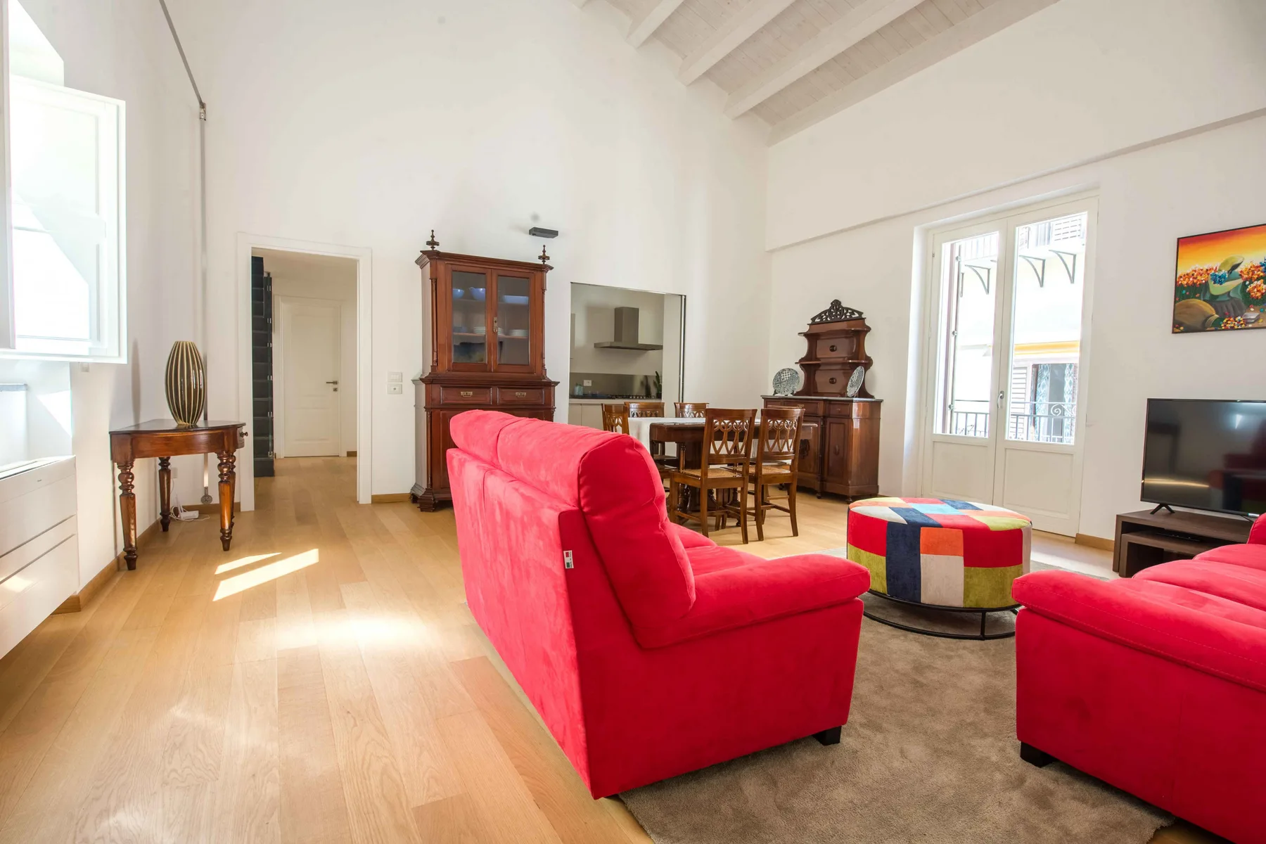 A bright living and dining room with red seating and a wooden dining table.