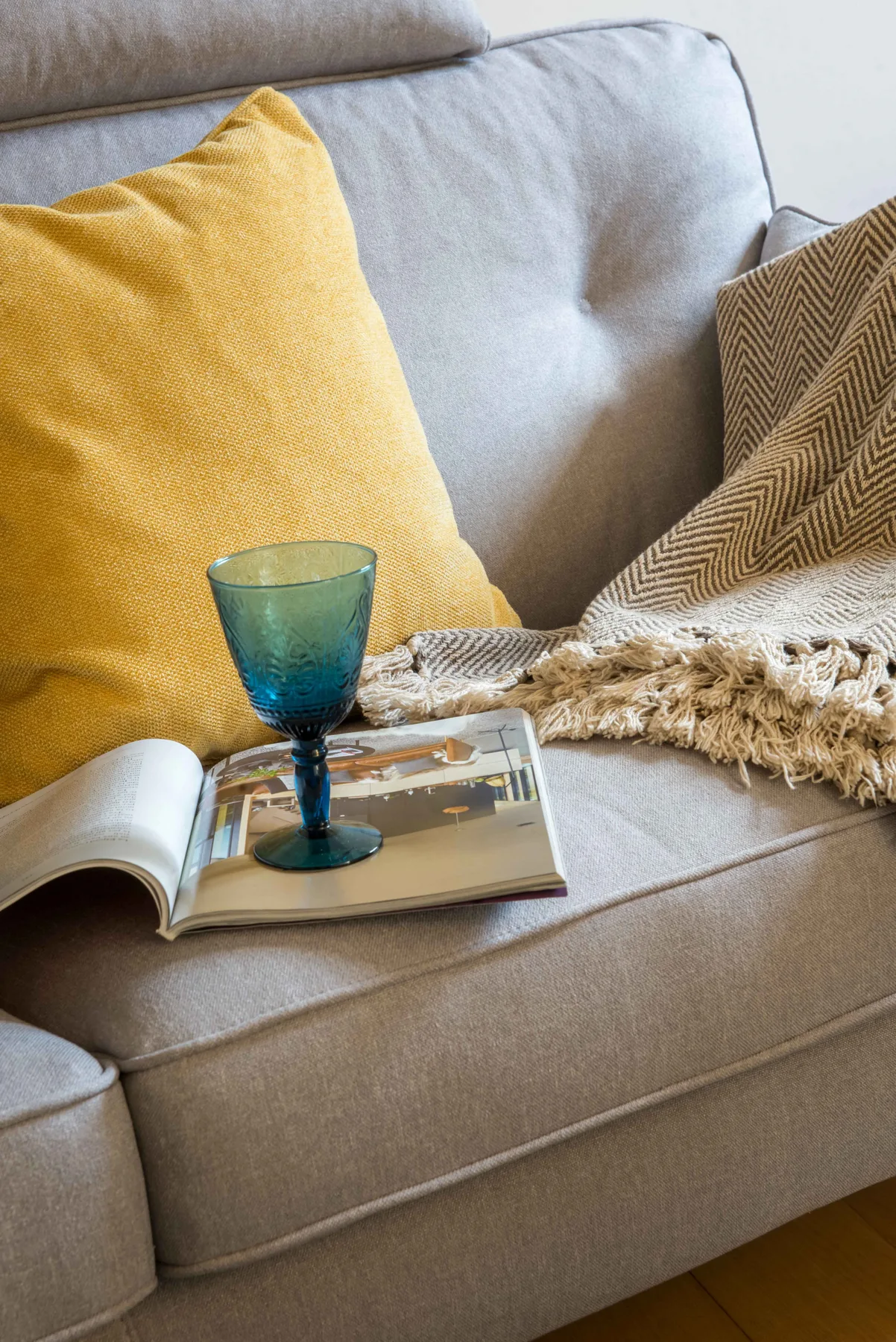 Una zona de estar con un cojín amarillo, un libro abierto y un vaso azul.