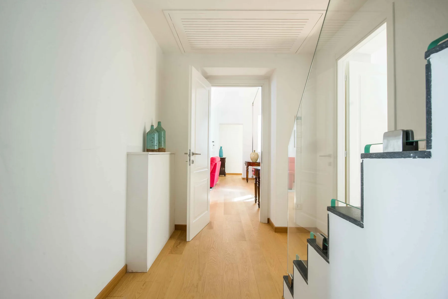 Un pasillo luminoso con suelo de madera clara conduce a una puerta abierta.
