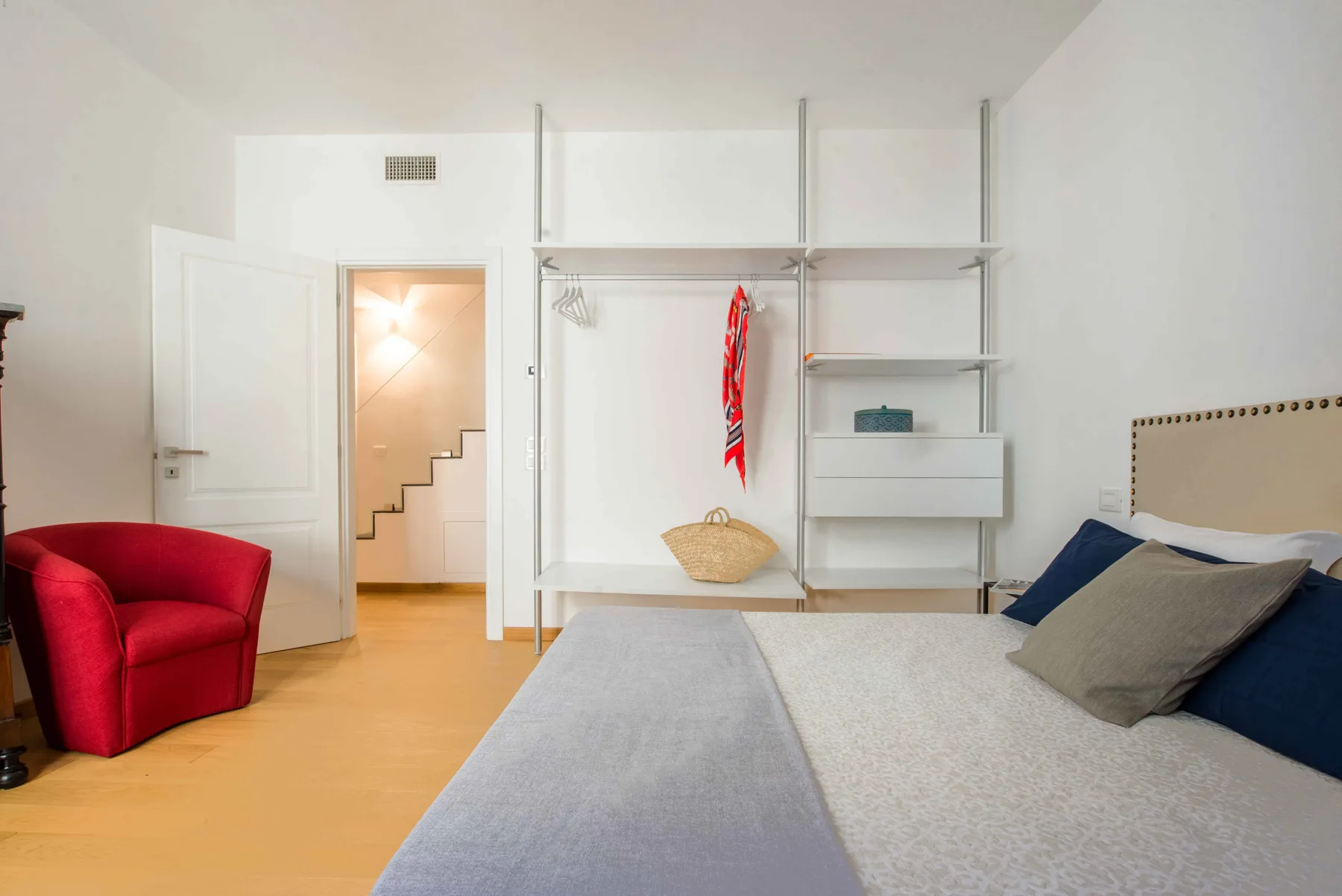 Un dormitorio con una cama, un sillón rojo y un armario abierto.