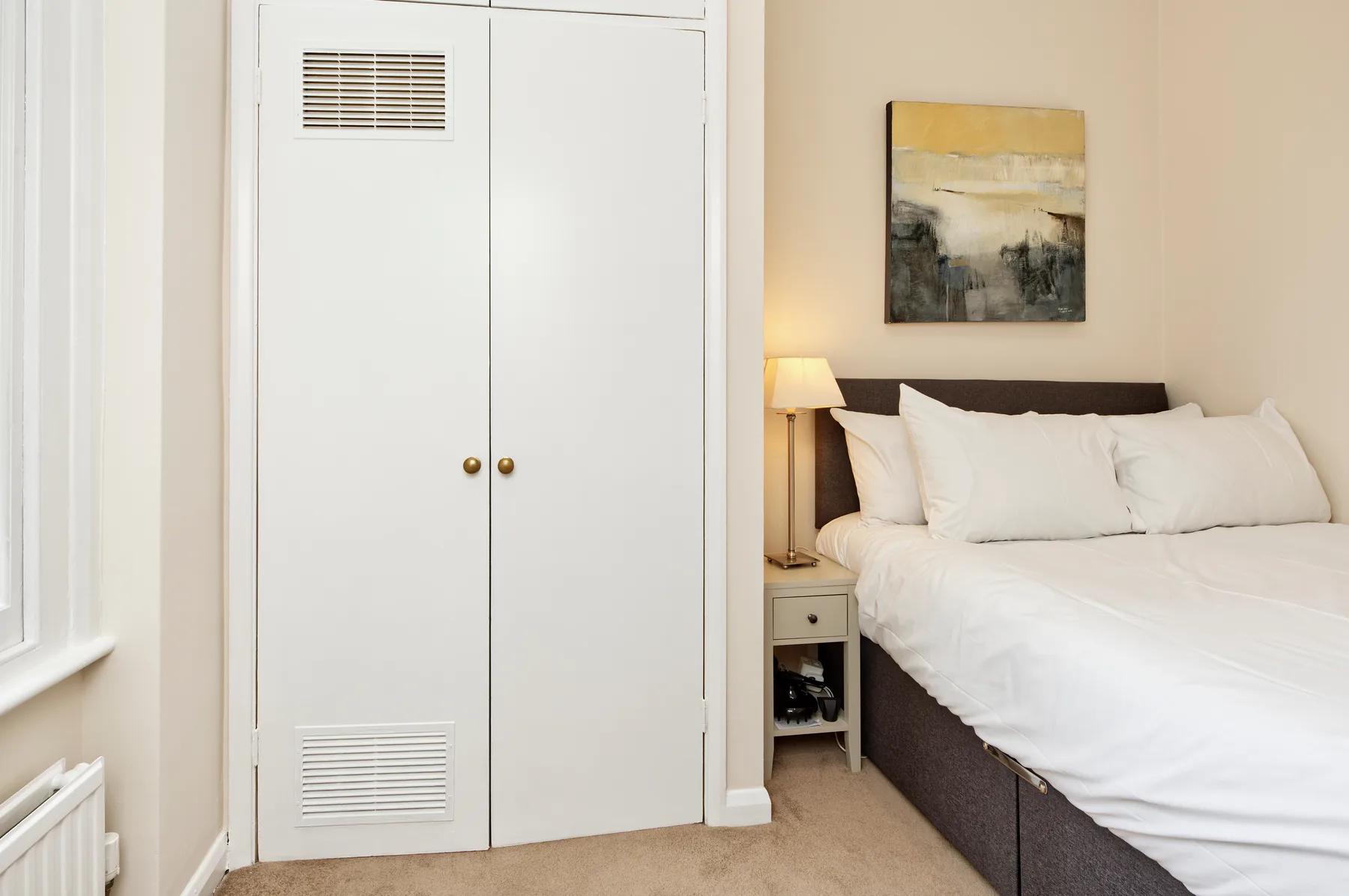 Un dormitorio con una cama, un armario blanco y una lámpara de noche.