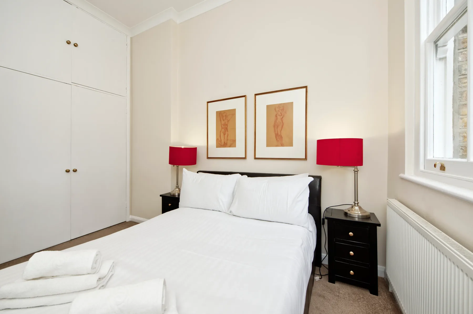 Un dormitorio luminoso con una cama bien arreglada y lámparas rojas junto a la cama.