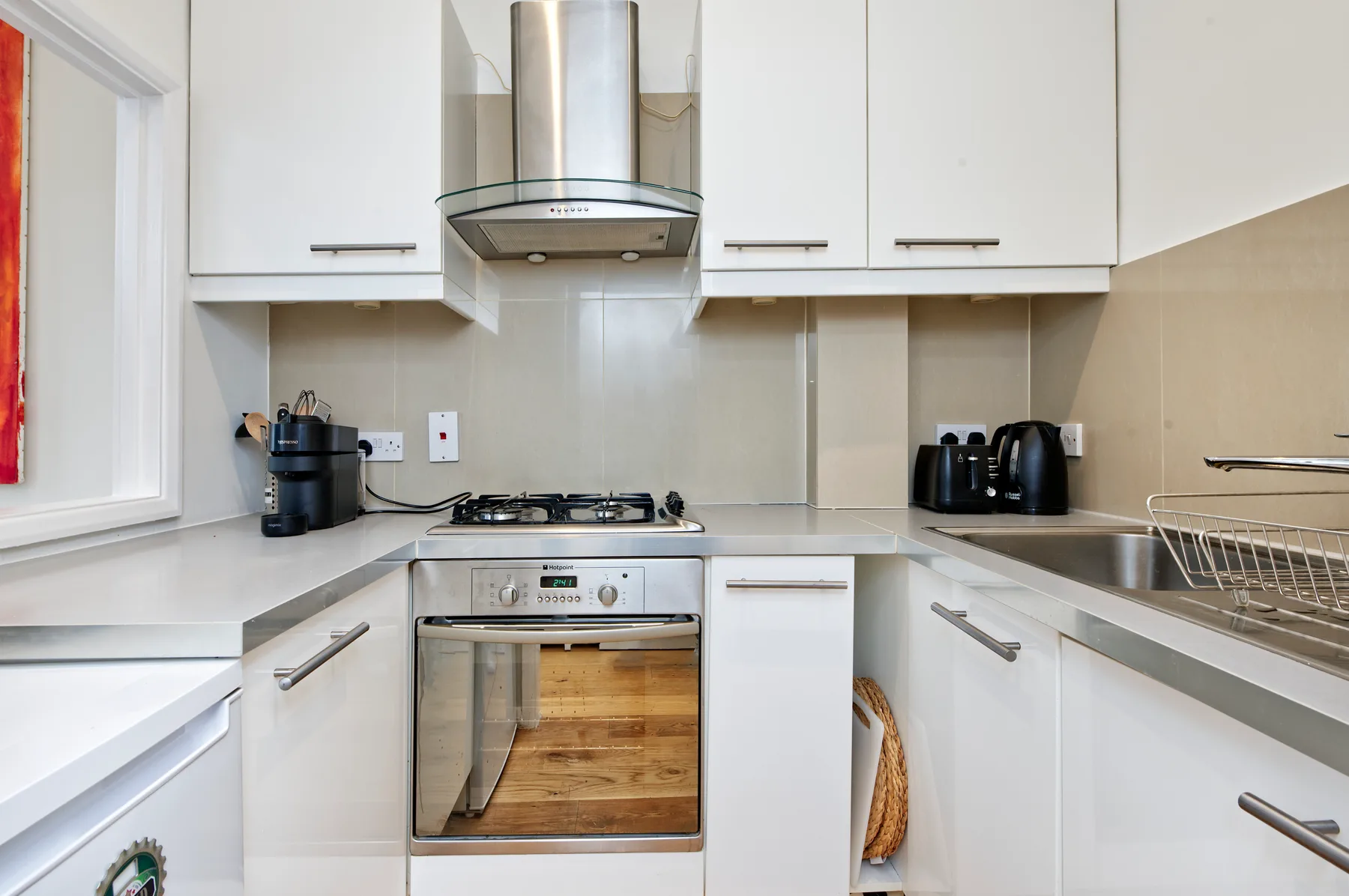 Una cocina luminosa con gabinetes blancos, estufa y campana extractora de acero inoxidable.