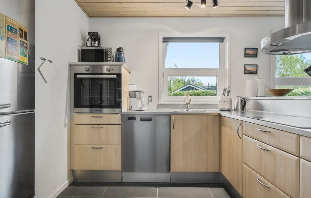 Una cocina luminosa con gabinetes de madera clara, electrodomésticos de acero inoxidable y una ventana sobre el fregadero.