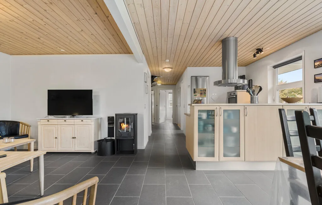 Una sala y cocina diáfanas con techos de madera clara y suelos de baldosas oscuras.