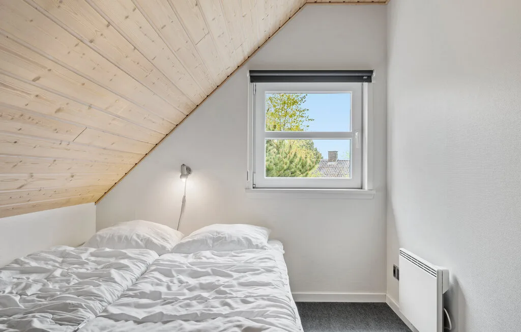 Un dormitorio con una cama bajo un techo inclinado y una ventana.