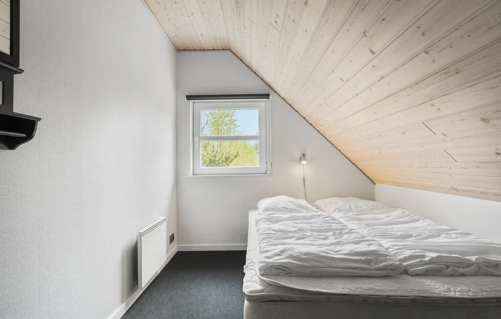 Un dormitorio con una cama bajo un techo inclinado de madera y una ventana pequeña.