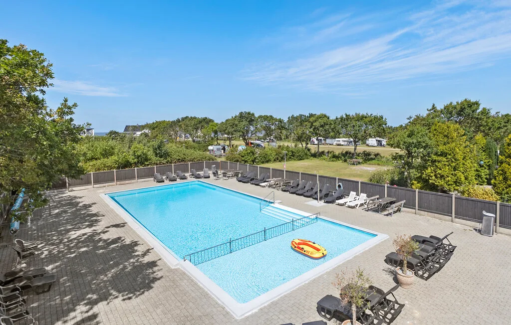 Una piscina al aire libre está rodeada de tumbonas y una terraza pavimentada.