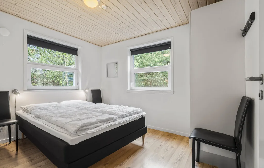 Un dormitorio luminoso con una cama bajo dos ventanas.