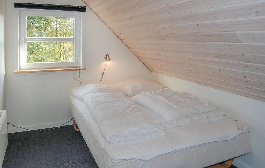 Un dormitorio con una cama bajo un techo inclinado y una ventana.