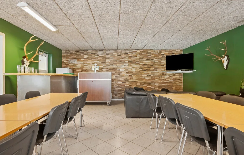 Una sala de reuniones con mesas largas, sillas y un televisor en la pared.