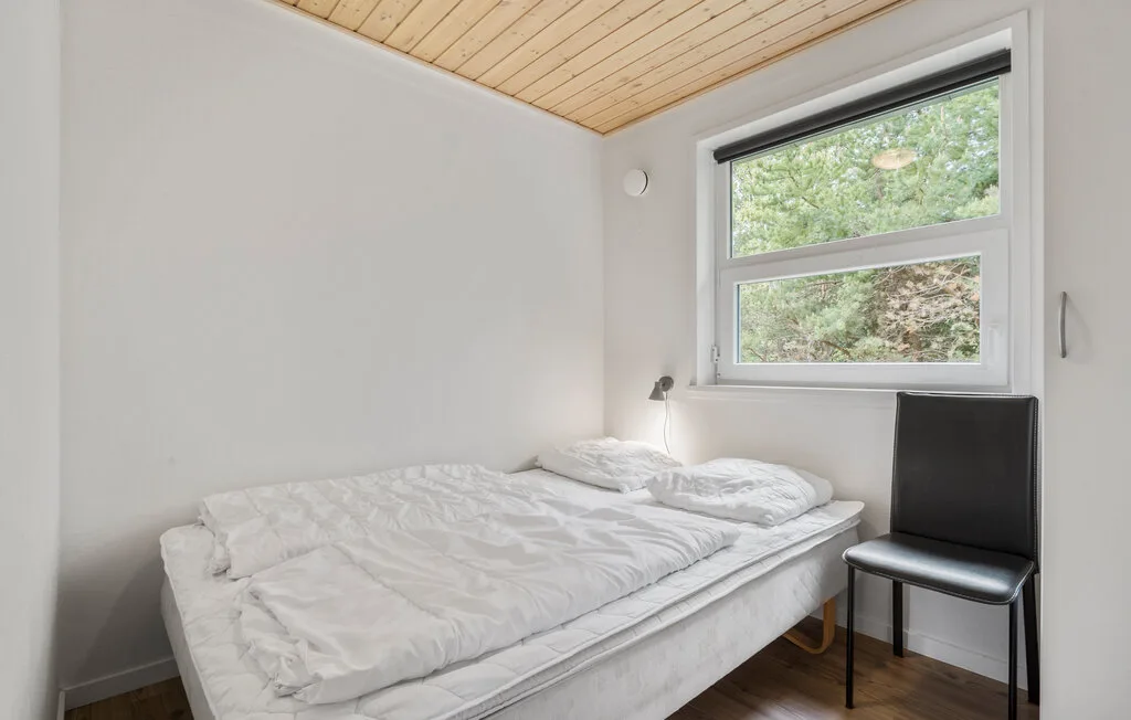 Un dormitorio con una cama bajo una ventana y una silla al lado.