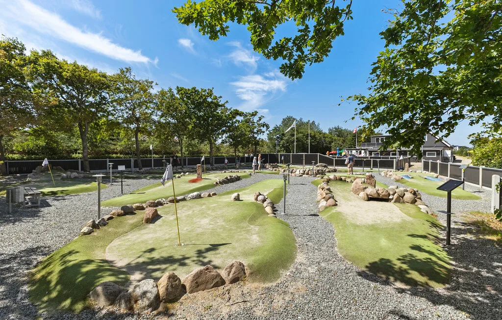 Un campo de minigolf al aire libre tiene greens ajardinados y bordes de piedra.