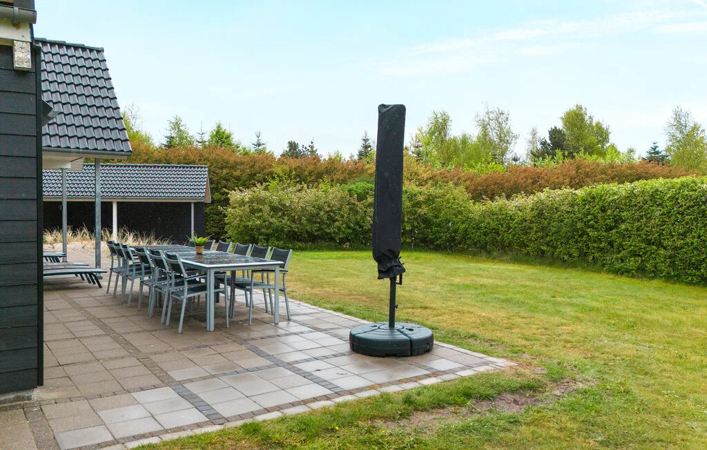 Un patio al aire libre con mesas y asientos junto a un jardín con césped.