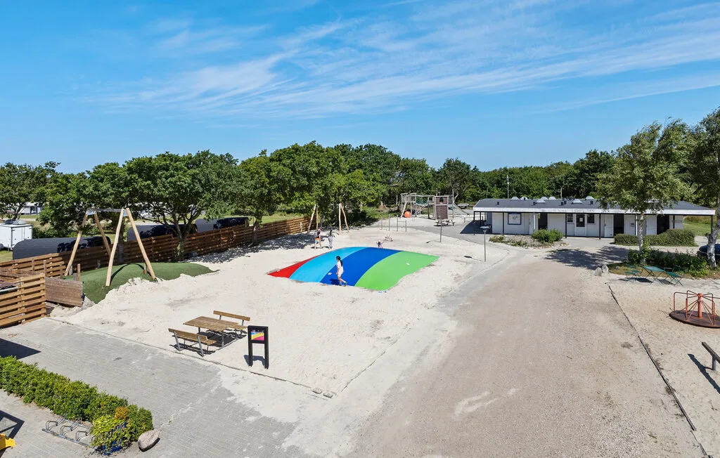 Un parque infantil al aire libre tiene una superficie de salto colorida, columpios y un edificio bajo.