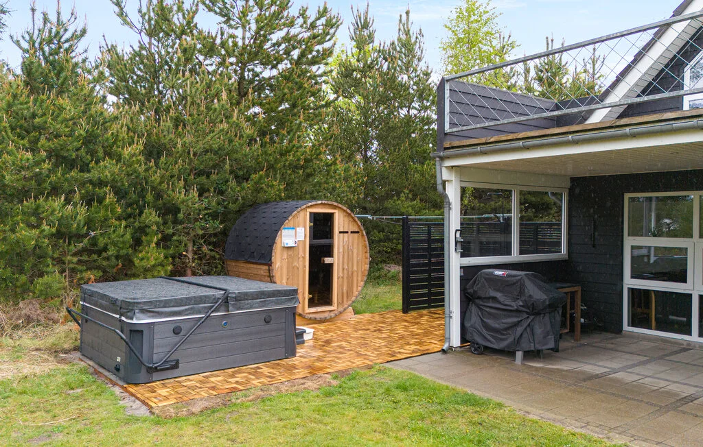Un patio exterior con una bañera de hidromasaje, una sauna de barril y una zona de estar cubierta.