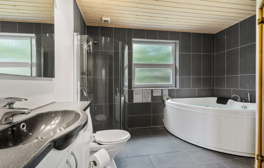 Un baño con azulejos, bañera, ducha, lavabo y ventana.