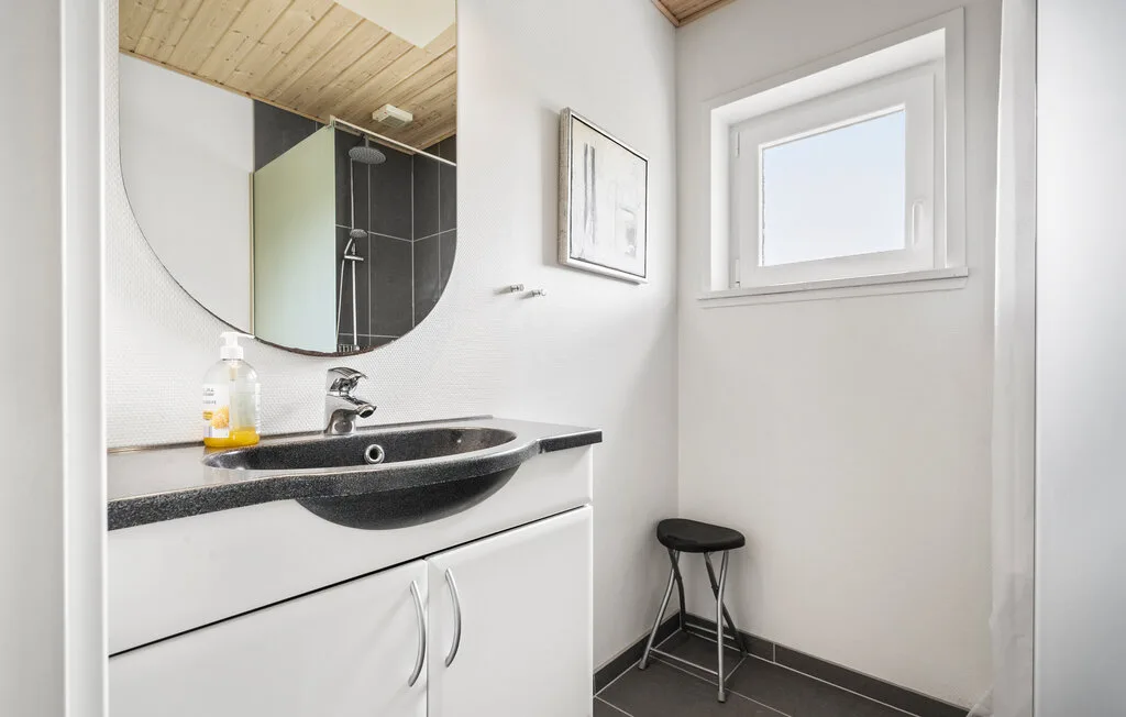 Un baño luminoso con lavabo, espejo y una ventana pequeña.