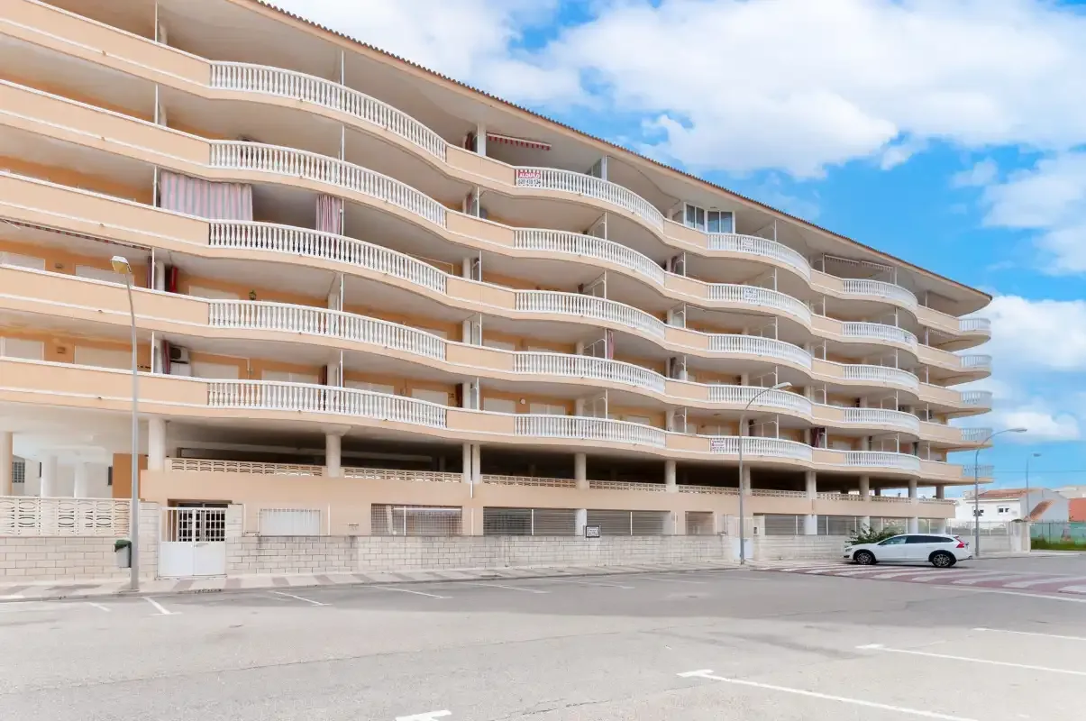 A curved apartment building with balconies stands beside a paved street.