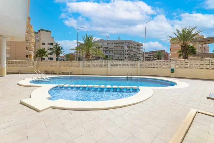 An outdoor swimming pool sits in a paved courtyard surrounded by apartment buildings.