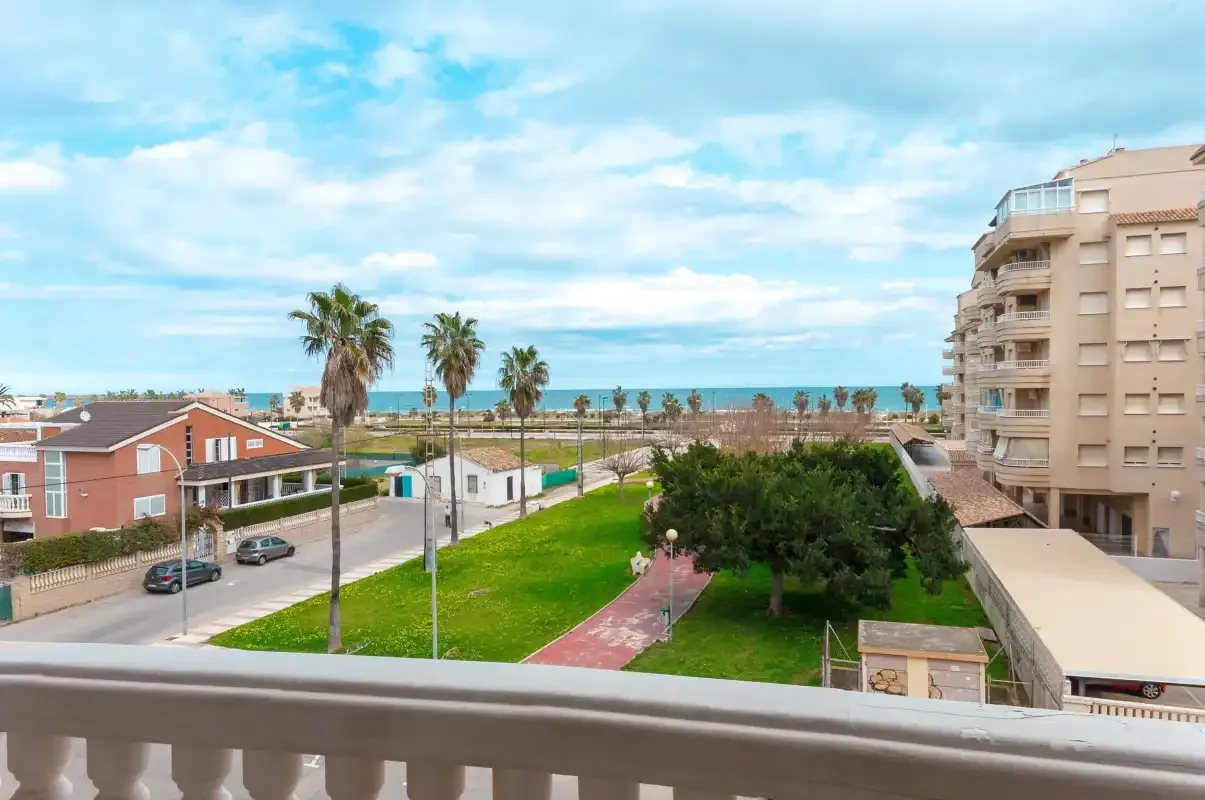 A balcony overlooks a landscaped green area, nearby buildings, and the sea.