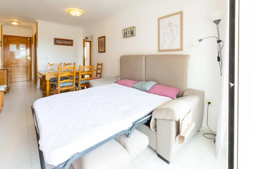A bright living and dining area with a bed, seating, and a wooden dining table.