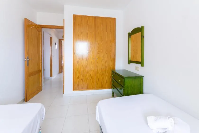 A bright bedroom with two beds, wooden doors, and a green dresser.