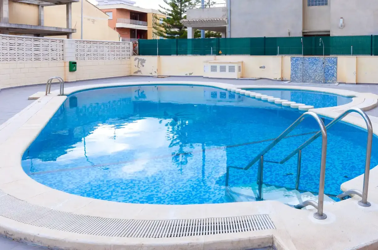 An outdoor swimming pool with metal handrails and surrounding residential buildings.
