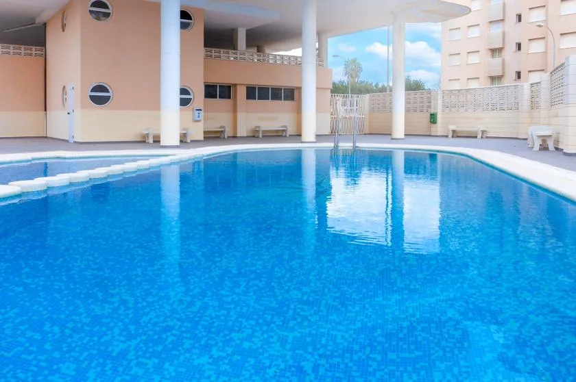 An outdoor swimming pool beside a pale building, with columns along the poolside.